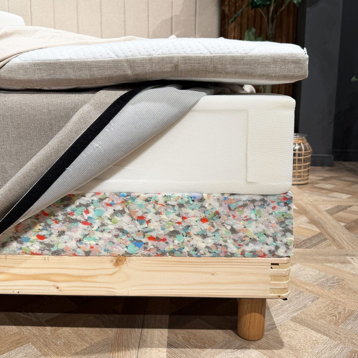 An der Bettecke freigelegte Schichten: Topper, Federkernmatratze mit geöffnetem Bezug und Schaumstoffkante des Bettunterbaus über dem Holzrahmen