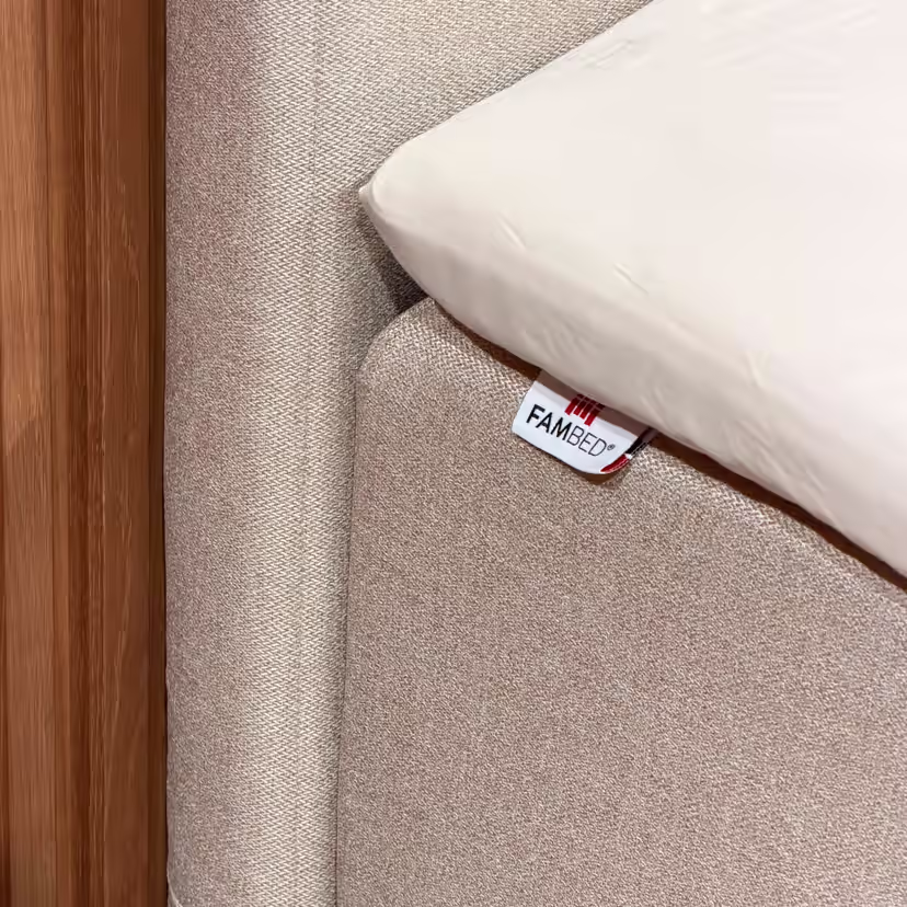 Nahaufnahme des beigen Bezugs um die Bettecke, mit FAMBED-Etikett und weissem Laken darüber